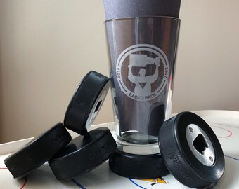 May include: Four black hockey pucks, one with a bottle opener, and a clear glass with a white design that says "2016 Back 2 Back 2017".