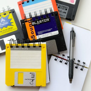 May include: A collection of vintage floppy disks and small notebooks with spiral bindings. The floppy disks are labeled with the text "Sound Blaster", "IMATION", and "MF-2HL".
