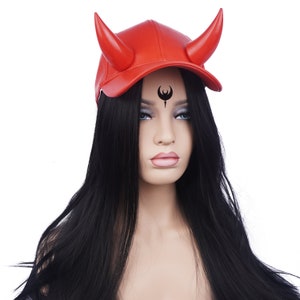 May include: A red baseball cap with two large, curved horns. The cap is made of a smooth material and has a curved brim. The horns are a darker shade of red. The cap is on a mannequin with long black hair.