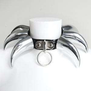 May include: A black leather choker with silver spikes. The choker has a silver ring attached to it.
