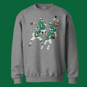 May include: A gray sweatshirt with a pixelated design of four football players in green and white uniforms. The players are in various poses, including throwing a football and running.