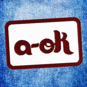 May include: A red embroidered patch with the text "a-ok" on a white background. The patch is surrounded by a red border.