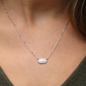 May include: A silver chain necklace with a white oval pendant set with small clear stones.