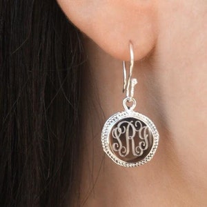 May include: Silver dangle earrings with a round, clear glass charm featuring a monogram of the letters "SRY".