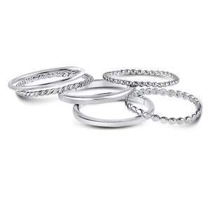 Puede incluir: Un conjunto de cinco anillos de tono plateado con diversas texturas, incluyendo bandas lisas, un dise&ntilde;o de cuerda trenzada y una banda con cuentas. Los anillos est&aacute;n dispuestos en grupo, mostrando su acabado met&aacute;lico y patrones.