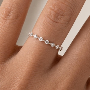 Peut inclure: Une fine bague en métal argenté ornée d'une série de petites pierres rondes et transparentes à facettes, disposées en rangée continue sur le dessus. Les pierres sont maintenues par de petites griffes, offrant un aspect délicat et brillant.