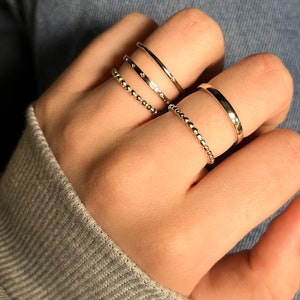 Puede incluir: Un conjunto de cinco anillos de tono plateado usados en los dedos. La colecci&oacute;n incluye dos bandas delgadas con cuentas, una banda lisa pulida, una banda con superficie plana y una banda delgada con peque&ntilde;as piedras claras incrustadas.