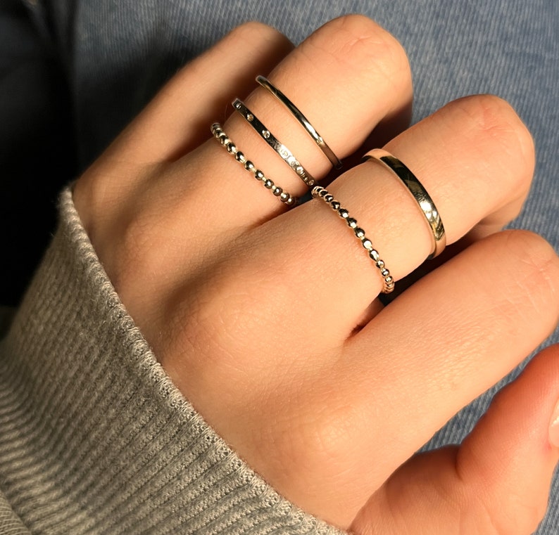 Puede incluir: Un conjunto de cinco anillos de tono plateado usados en los dedos. La colecci&oacute;n incluye dos bandas delgadas con cuentas, una banda lisa pulida, una banda con superficie plana y una banda delgada con peque&ntilde;as piedras claras incrustadas.