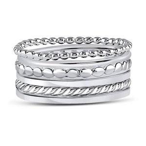 Puede incluir: Un conjunto de cuatro anillos de tono plateado. El anillo superior presenta una textura de cuentas delicadas, el segundo tiene cuentas lisas m&aacute;s grandes, el tercero muestra un patr&oacute;n de cuerda trenzada y el inferior es una banda lisa pulida.