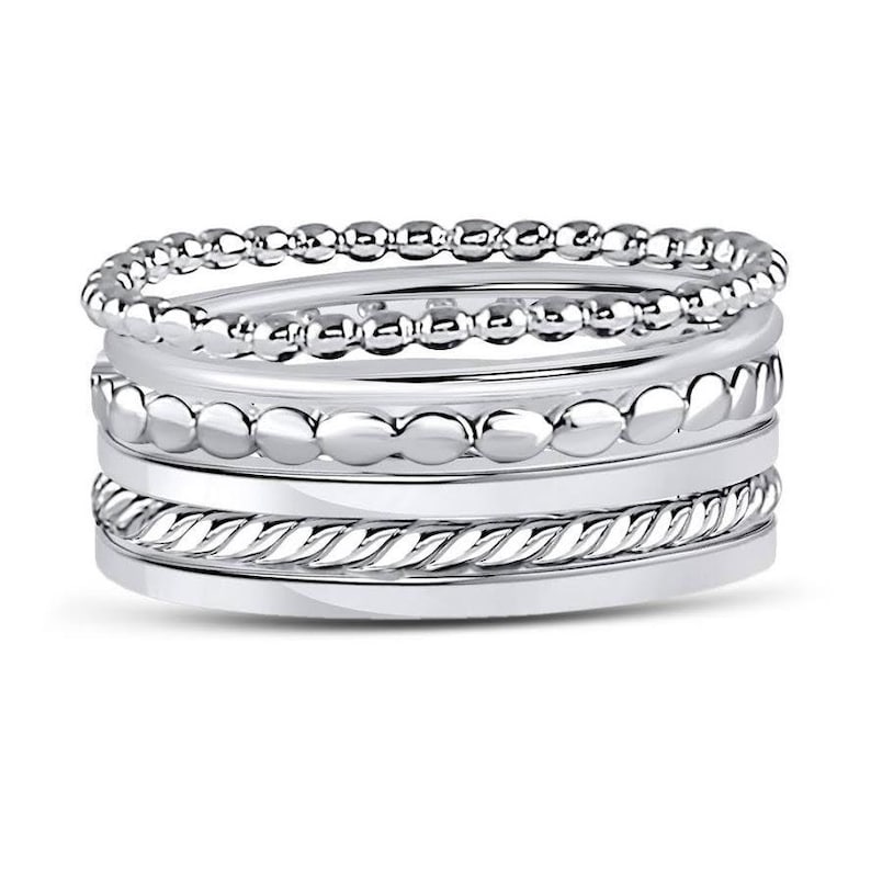 Puede incluir: Un conjunto de cuatro anillos de tono plateado. El anillo superior presenta una textura de cuentas delicadas, el segundo tiene cuentas lisas m&aacute;s grandes, el tercero muestra un patr&oacute;n de cuerda trenzada y el inferior es una banda lisa pulida.