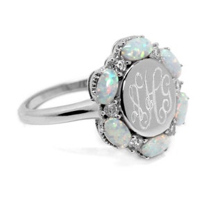 May include: A silver ring with a round, engraved monogram surrounded by a halo of white opals.