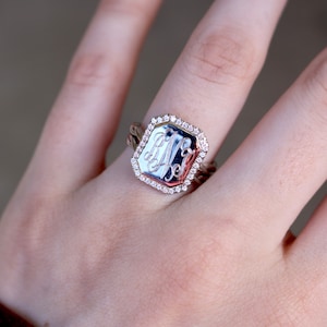 Peut inclure: Une bague en argent avec un visage carré serti de petites pierres claires. Le visage de la bague porte un monogramme gravé.