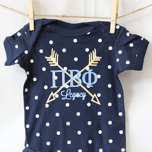 May include: A navy blue baby onesie with white polka dots and a gold and blue design that says "ПВФ Legacy".