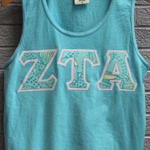 May include: A turquoise tank top with a white and green patterned "ZTA" design on the front.
