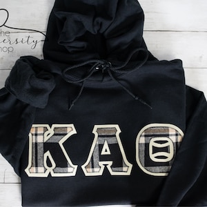 May include: Black hooded sweatshirt with a large plaid "KAO" design on the front.