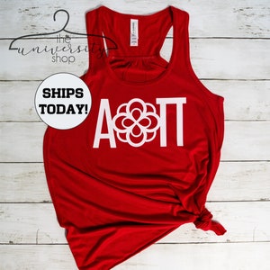 May include: Red tank top with a white graphic of the letters A and T with a circle design in between. The letters are in a large, bold font.