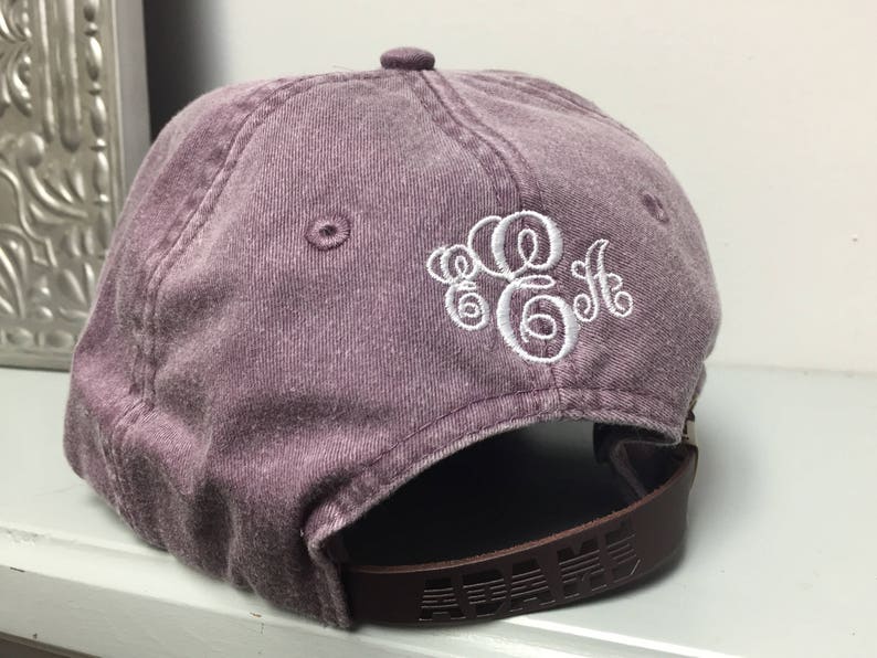 Op de afbeelding: Een paarse, verweerde, katoenen baseballpet met een wit geborduurd monogram. De pet heeft een bruin verstelbaar bandje.