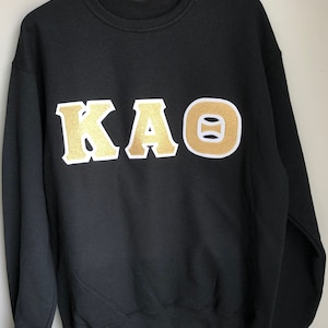 May include: Black sweatshirt with gold Greek letters "KAΘ" on the front.