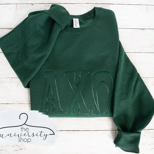 May include: A dark green sweatshirt with the letters "AXO" embroidered in a raised, outlined style.