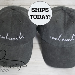 May include: Two gray baseball caps with white embroidered text. The cap on the left says "cool uncle" and the cap on the right says "cool aunt".