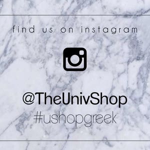Op de afbeelding: Witte marmeren achtergrond met een zwart Instagram-pictogram en tekst die "find us on instagram @TheUnivShop #ushopgreek" luidt.