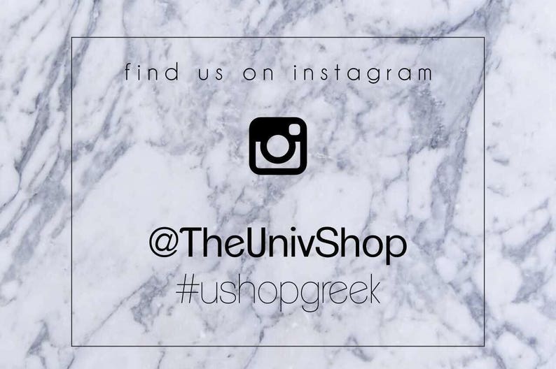 Op de afbeelding: Witte marmeren achtergrond met een zwart Instagram-pictogram en tekst die "find us on instagram @TheUnivShop #ushopgreek" luidt.