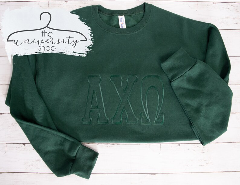 May include: A dark green sweatshirt with the letters "AXO" embroidered in a raised, white outline.