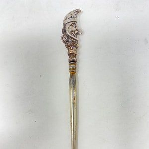 May include: A silver shoe horn with a detailed, whimsical face on the handle. The face has a pointed hat and a mischievous expression.