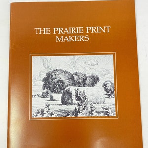 May include: A brown booklet with the title "The Prairie Print Makers" in white text. The cover features a black and white illustration of a field with hay bales and trees.