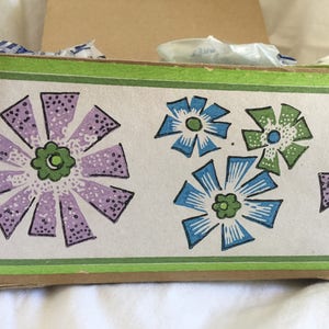 May include: A brown cardboard box with a green and white floral design. The flowers are purple, blue, and green.