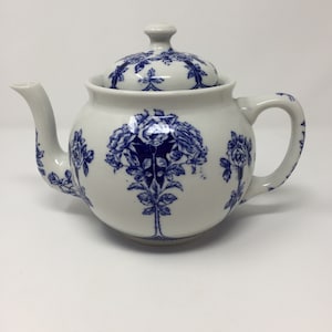 May include: A white teapot with a blue floral design. The teapot has a lid and a handle. The floral design features roses and leaves.