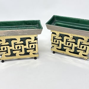 May include: Two decorative rectangular containers. Each has a green interior, a silver-colored rim, and a gold-colored, openwork base. The containers are elevated on small black feet. The design is geometric and vintage.