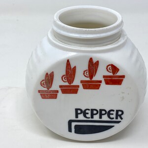 May include: White ceramic pepper shaker with a black and white knife graphic and the word "PEPPER" printed on the bottom. The shaker has a ribbed design and features a red and white graphic of four potted plants.