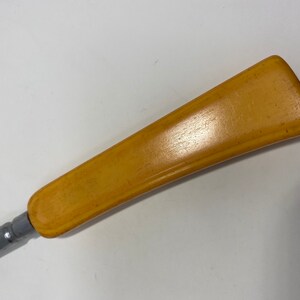 May include: A close-up of a yellow plastic handle attached to a metal tool. The handle is smooth and has a slight curve.