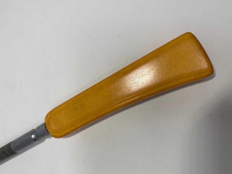 May include: A close-up of a yellow plastic handle attached to a metal tool. The handle is smooth and has a slight curve.