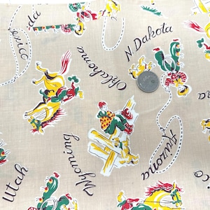 May include: Tan fabric with a repeating pattern of cowboys, horses, and cacti in red, yellow, green, and white. The names of several states are written in black script, including Arizona, Oklahoma, and Wyoming. A U.S. quarter is included for scale.