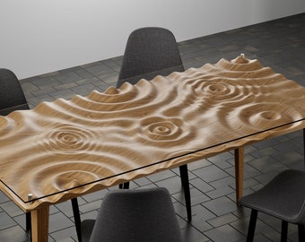 Puede incluir: Una mesa de comedor de madera con un diseño de superficie único y ondulado con círculos tallados. La mesa tiene una tapa de vidrio transparente y está rodeada de cuatro sillas grises.
