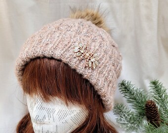May include: A pink knit beanie with a faux fur pom pom and a sparkly rhinestone embellishment.