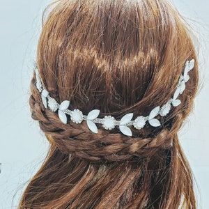 May include: A silver and white leaf-shaped hair comb with rhinestones. The comb is worn in a braided hairstyle.