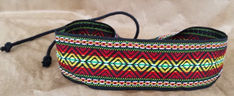 May include: A black woven belt with a colorful geometric pattern in red, yellow, green, and white. The belt has a long black cord that can be tied to adjust the fit.