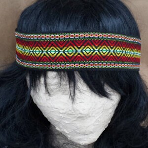 May include: A black headband with a colorful geometric pattern in red, yellow, green, and white. The headband is made of woven fabric and has a black backing.