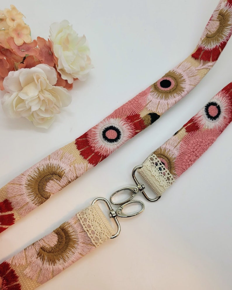 May include: A pink and red floral patterned fabric strap with a white lace trim and silver metal clasps. The strap is designed for a bag or purse.