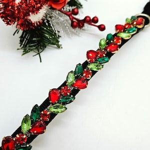 May include: A black velvet ribbon with red and green jewel-like embellishments. The ribbon is decorated with a repeating pattern of green and red stones.
