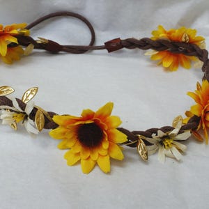 May include: A brown braided headband with yellow sunflowers and white flowers, accented with gold leaves.