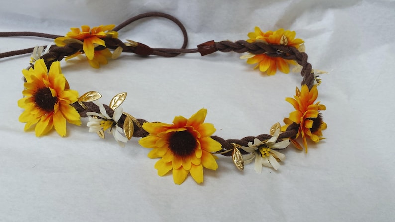 May include: A brown braided headband with yellow sunflowers and white flowers, accented with gold leaves.