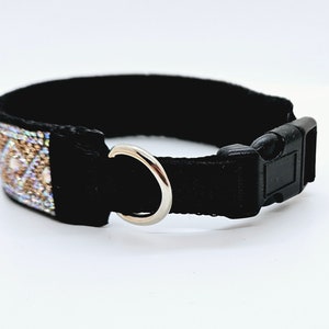 Puede incluir: Un collar de perro negro con un anillo en D plateado y una hebilla de pl&aacute;stico negro. El collar tiene una banda decorativa de lentejuelas y cuentas iridiscentes.