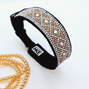 Puede incluir: Un collar de perro de terciopelo negro con un patr&oacute;n de diamantes de imitaci&oacute;n iridiscentes en forma de diamante en tonos dorados y transparentes. El collar tiene una hebilla plateada y el texto "Handmade MK" est&aacute; impreso en la parte posterior.
