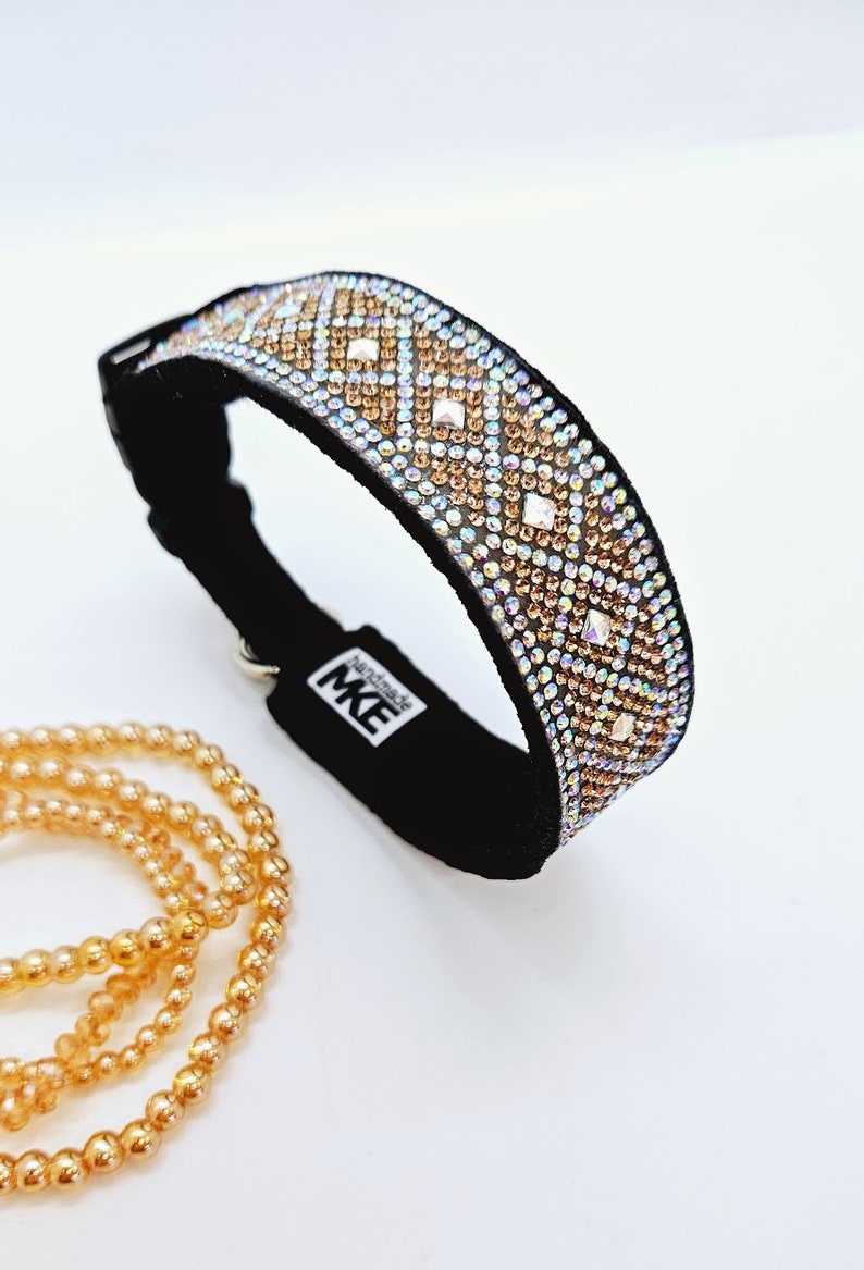 Puede incluir: Un collar de perro de terciopelo negro con un patr&oacute;n de diamantes de imitaci&oacute;n iridiscentes en forma de diamante en tonos dorados y transparentes. El collar tiene una hebilla plateada y el texto "Handmade MK" est&aacute; impreso en la parte posterior.