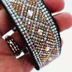 Puede incluir: Un brazalete de cuero negro con un patr&oacute;n geom&eacute;trico de diamantes de imitaci&oacute;n iridiscentes y dorados.
