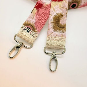 May include: A pink and brown floral fabric strap with white lace trim and silver metal clasps.